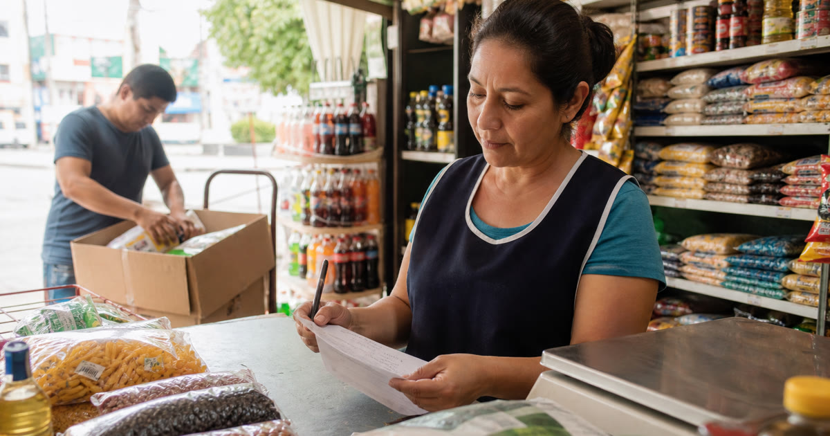 Dueño de una tienda de abarrotes revisando una lista de compra junto a productos en anaquel