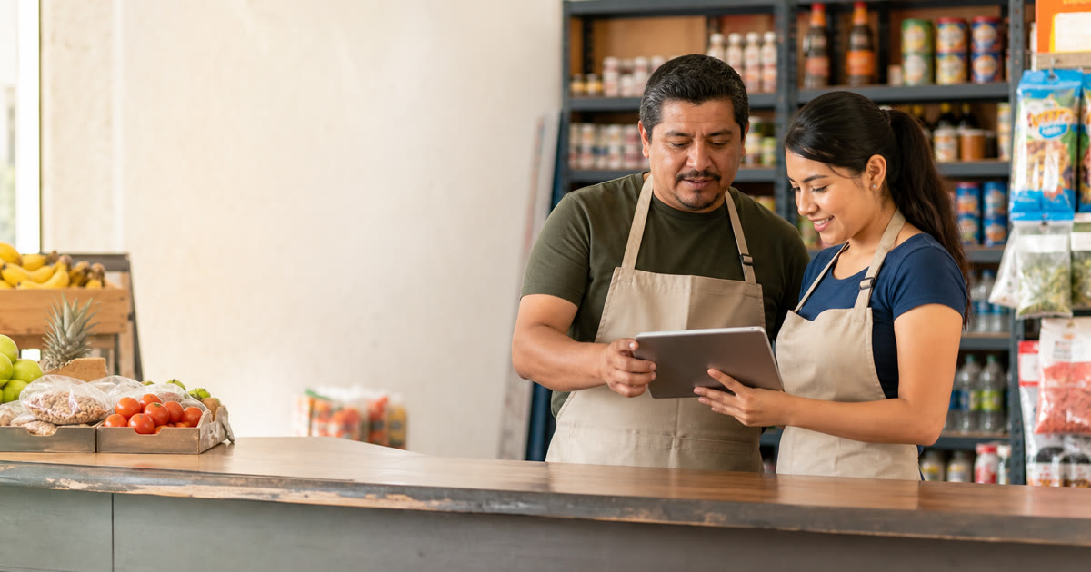 Dueño y cajera revisando una tablet junto al mostrador de una tienda de abarrotes